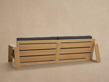 Close-up of Canyon Outdoor Teak Sofa, showing a light teak wood armrest and dark grey seat and back cushions.