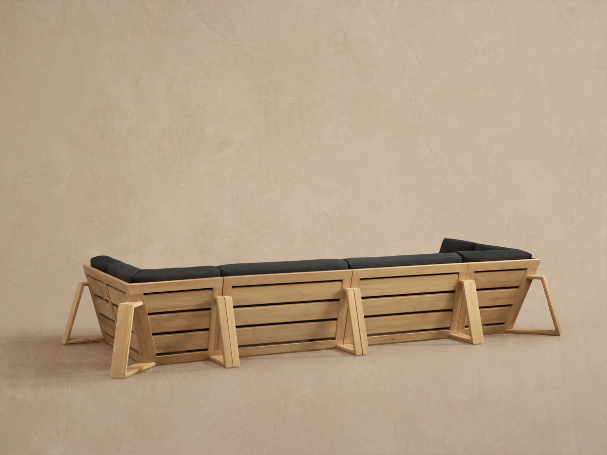Close-up of a Canyon Outdoor Teak Sectional. Natural teak frame with slatted side panels and dark gray cushions.
