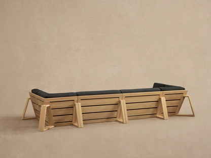 Close-up of a Canyon Outdoor Teak Sectional. Natural teak frame with slatted side panels and dark gray cushions.