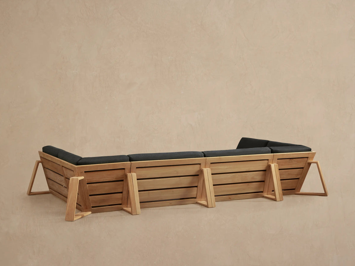 Angled close-up of Canyon Outdoor Teak Four-Piece Sectional, natural teak wood frame and dark grey cushions.