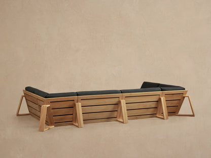 Angled close-up of Canyon Outdoor Teak Four-Piece Sectional, natural teak wood frame and dark grey cushions.
