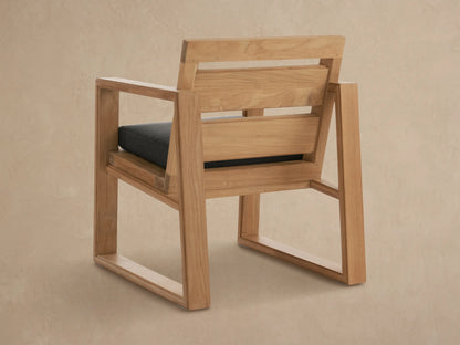Angled close-up of a Canyon Outdoor Teak Dining Arm Chair, featuring light natural teak wood and a dark gray seat cushion.