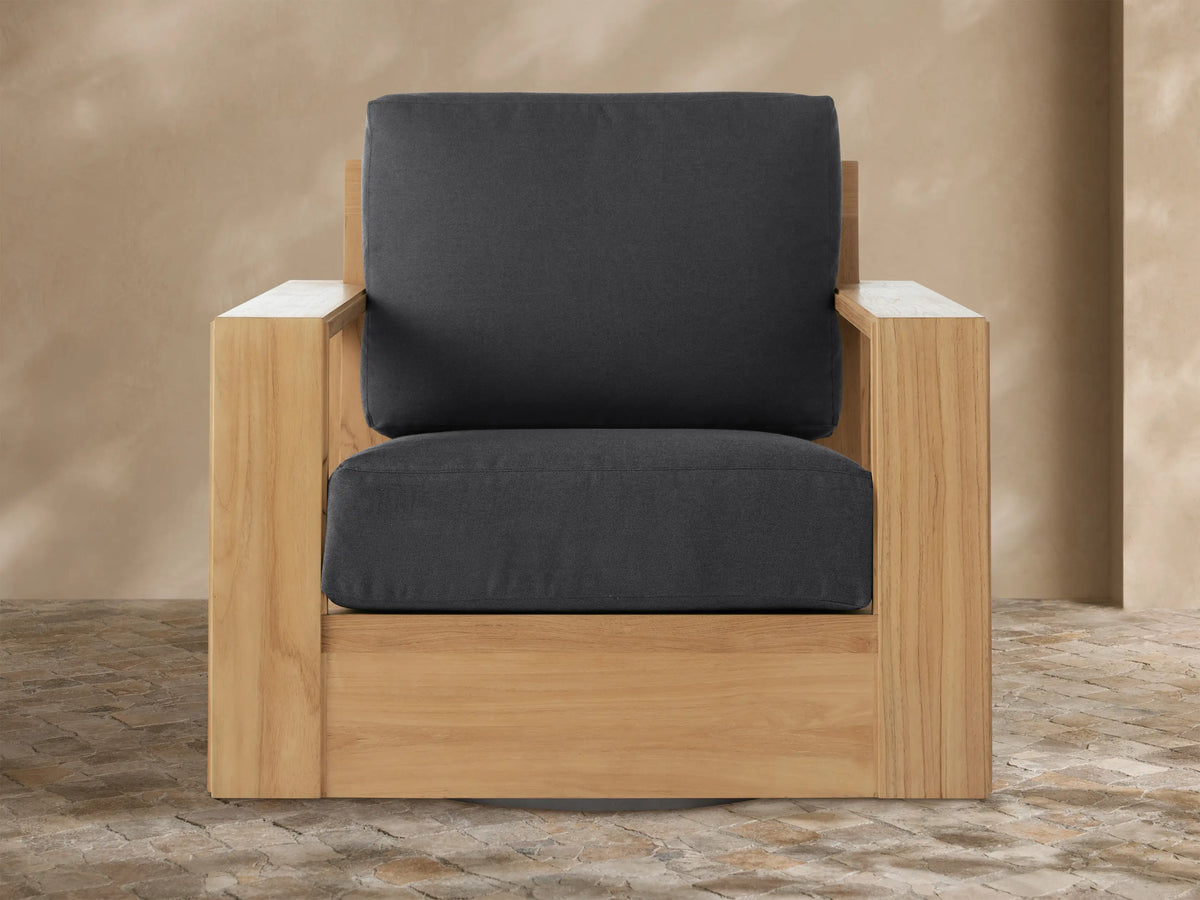 Canyon Outdoor Teak Swivel Chair with natural teak frame and dark grey cushions on a paved patio.