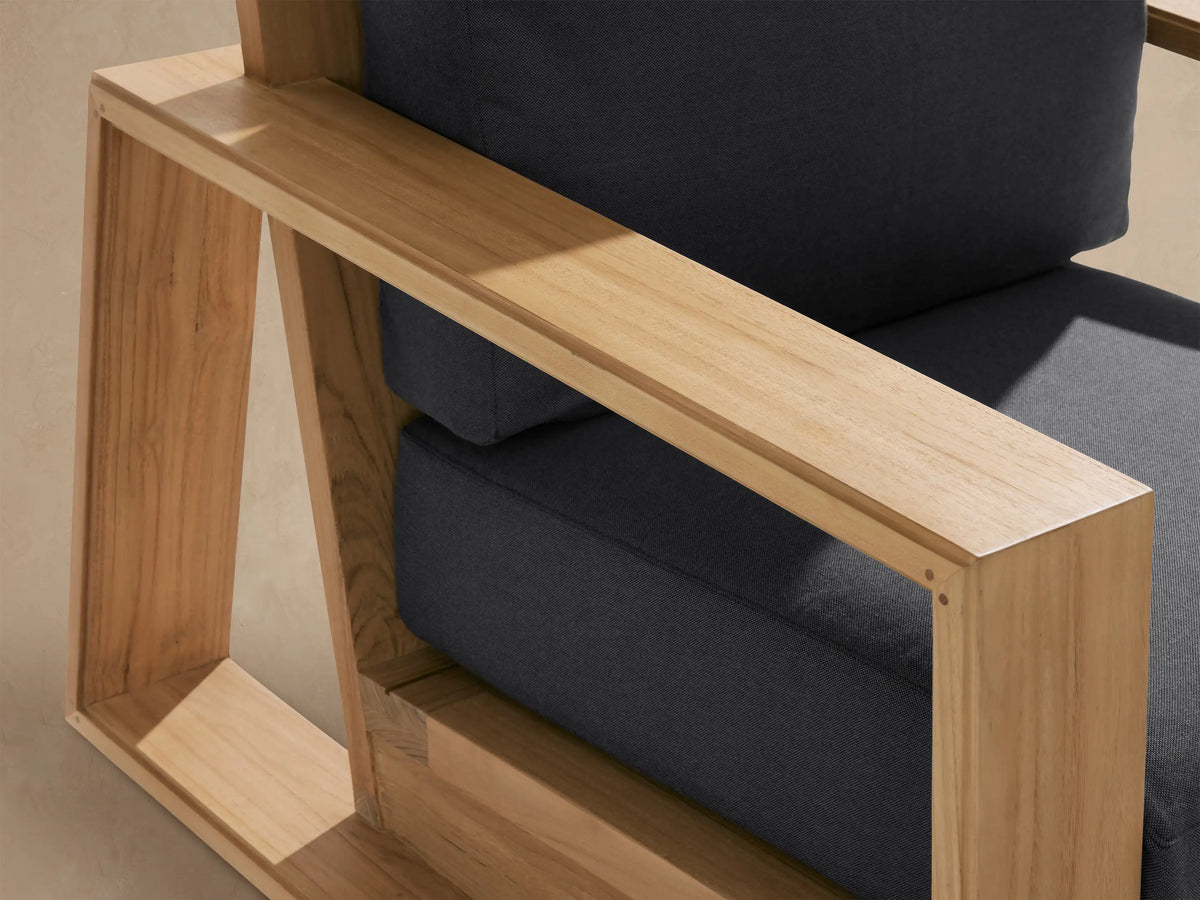 Front-facing Canyon Outdoor Teak Swivel Chair, natural teak wood frame with dark charcoal gray cushions on a tiled patio.