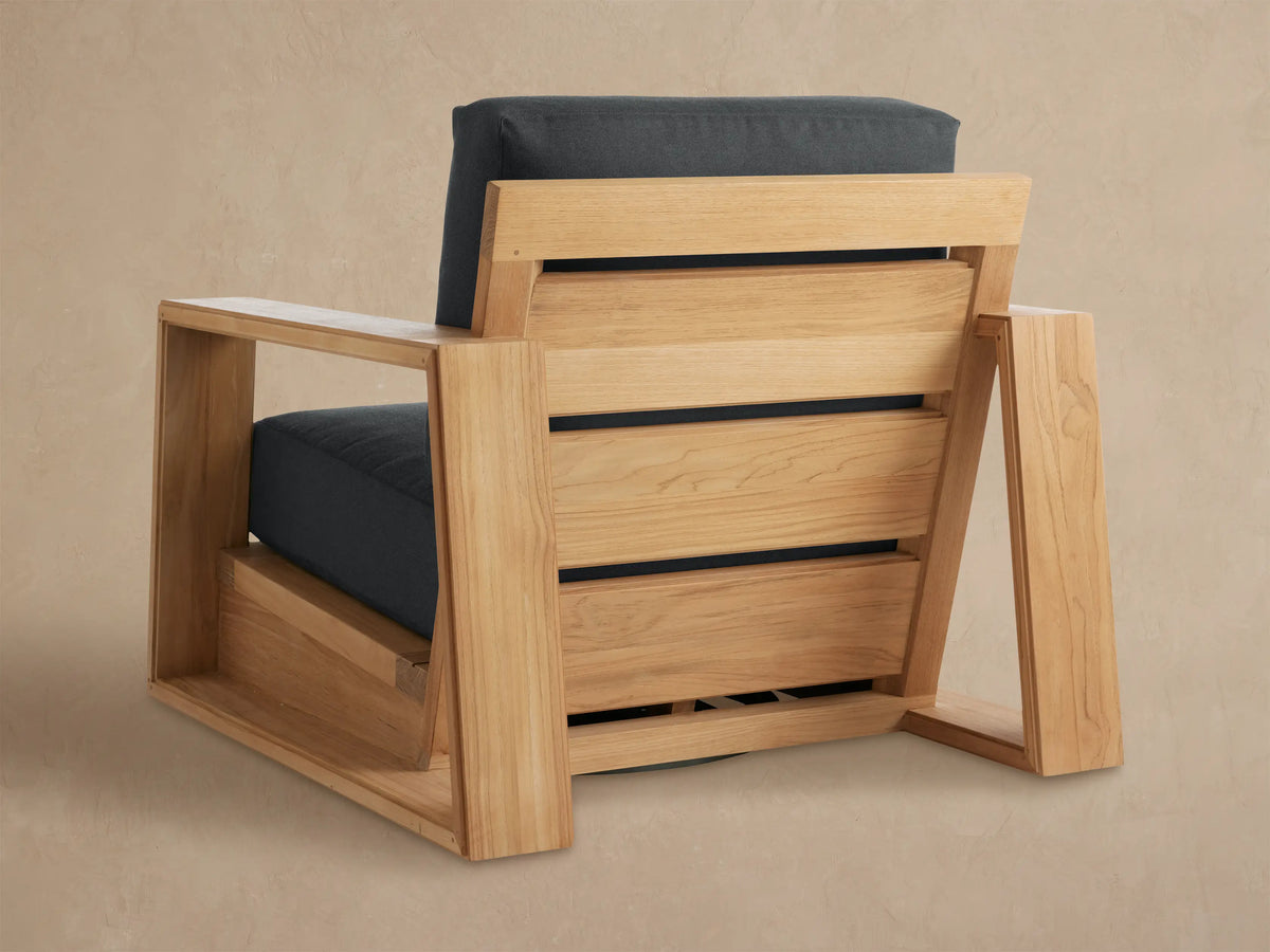 Angled close-up of the Canyon Outdoor Teak Swivel Chair, highlighting its light natural teak wood armrest and dark gray cushions.