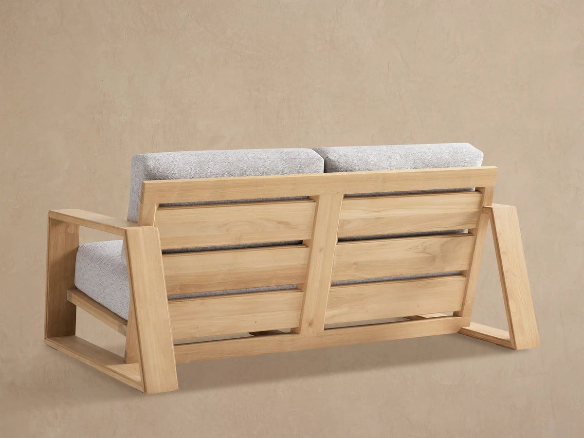Close-up of Canyon Outdoor Teak Sofa, showing its light brown teak wood frame and light grey fabric cushions.