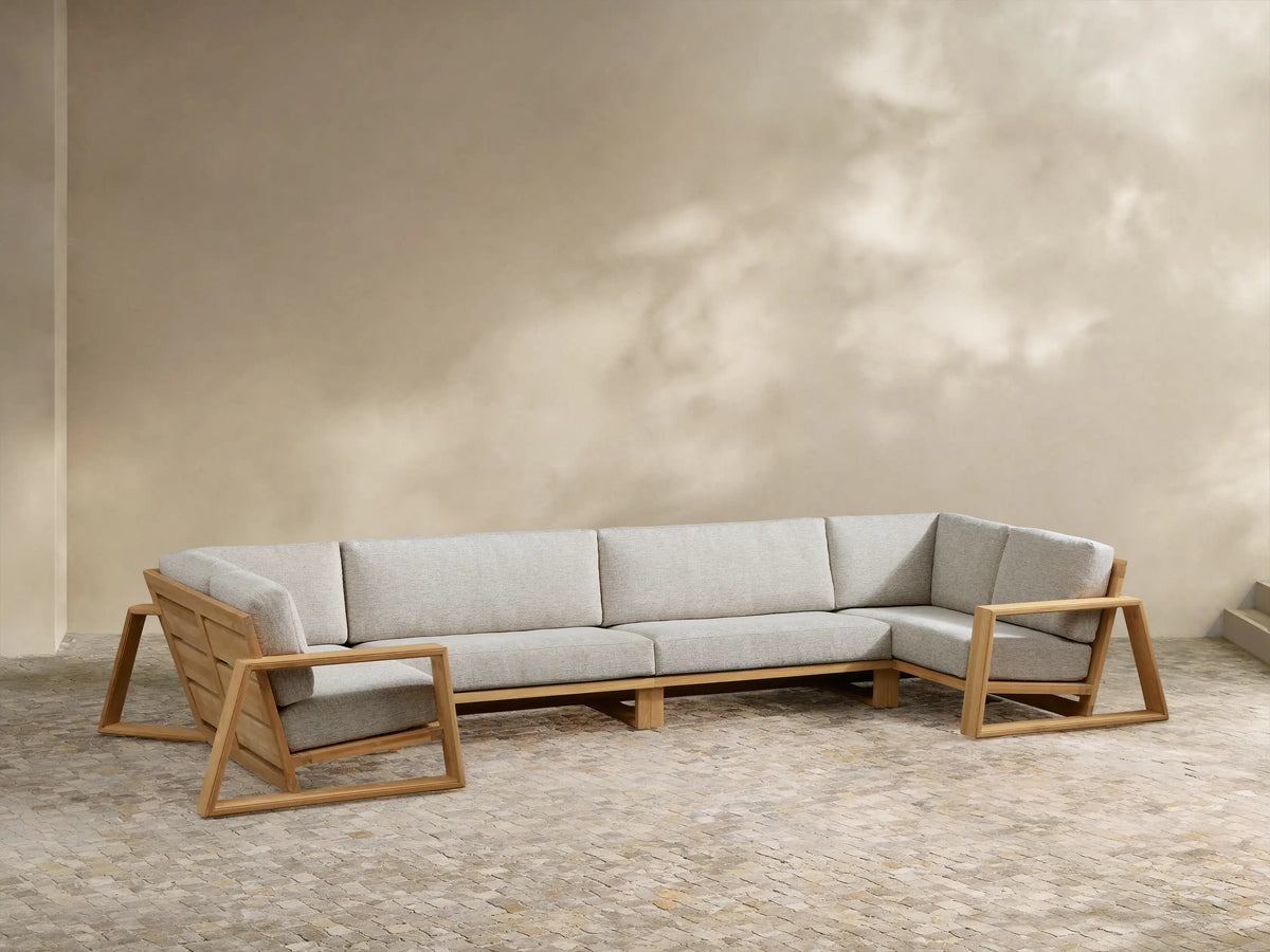 Canyon Outdoor Teak Sectional with natural wood frame, light grey cushions, arranged in a wide U-shape on a paved patio.
