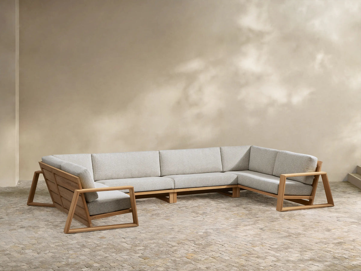 U-shaped Canyon Outdoor Teak Four-Piece Sectional with natural wood frame & light grey cushions on a patio.