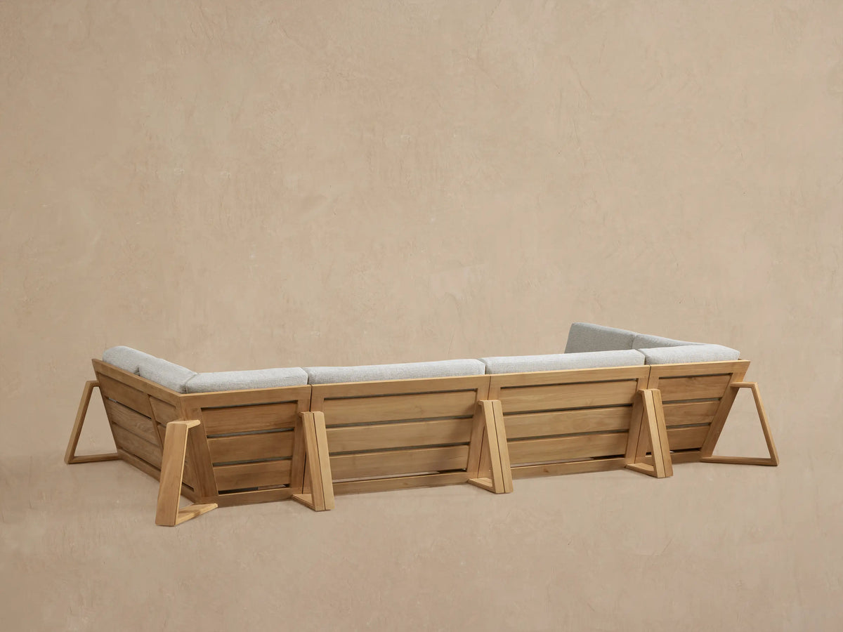 Angled close-up of the Canyon Outdoor Teak Sectional, showing a natural wood armrest and light gray textured cushions.