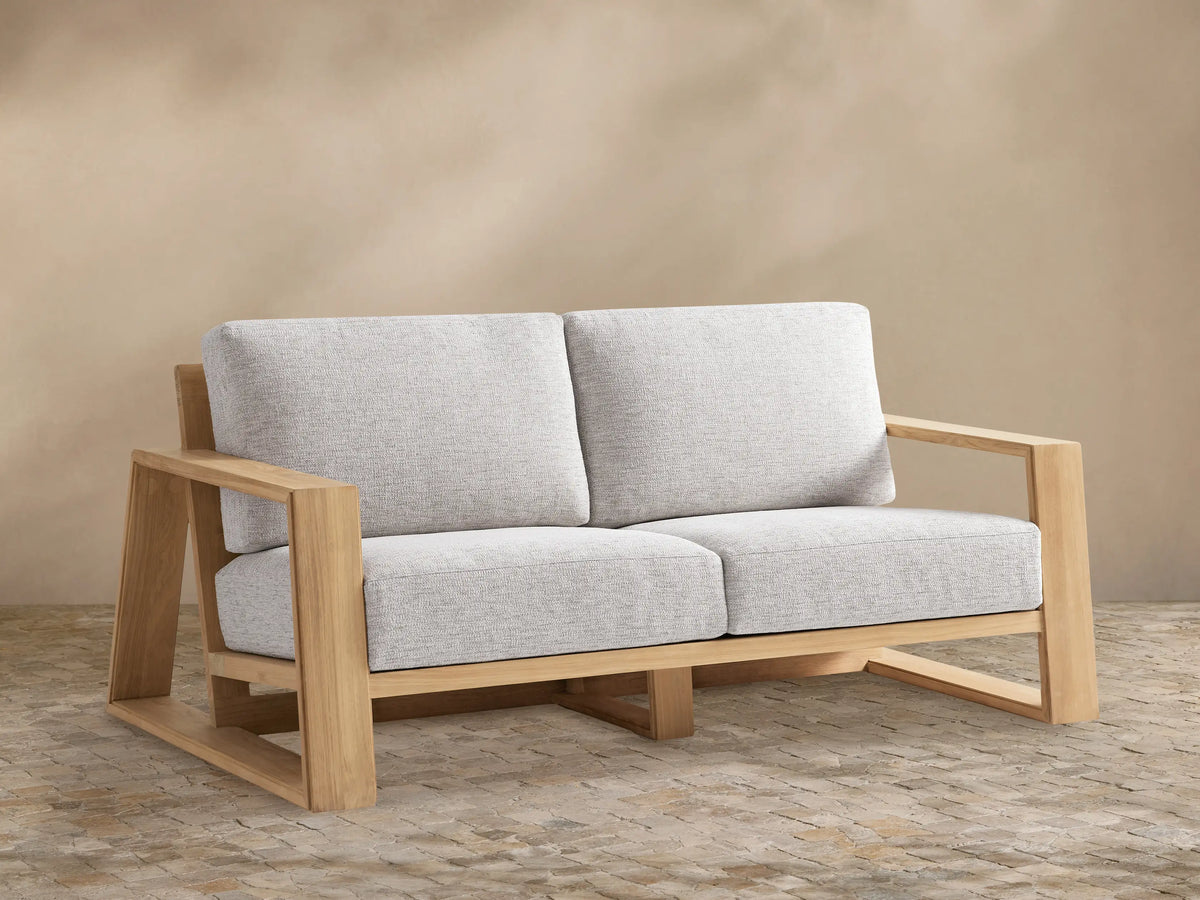 Canyon Outdoor Teak Sofa, a two-seater with light natural teak wood frame and plush light gray cushions, facing forward.