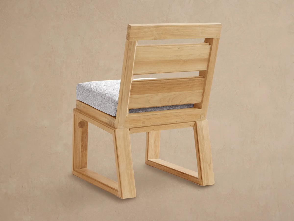 Angled close-up of a Canyon Outdoor Teak Dining Side Chair with light natural teak wood frame and a textured gray seat cushion.