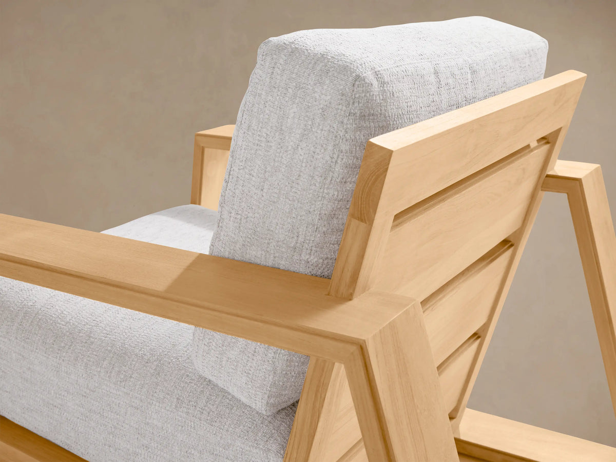 Front view of Canyon Outdoor Teak Lounge Chair with light natural teak wood frame and light grey cushions on stone patio.