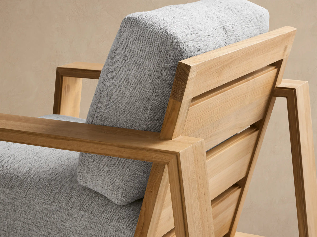 Canyon Outdoor Teak Swivel Chair, front view, with light gray cushions & natural teak frame on a textured patio.