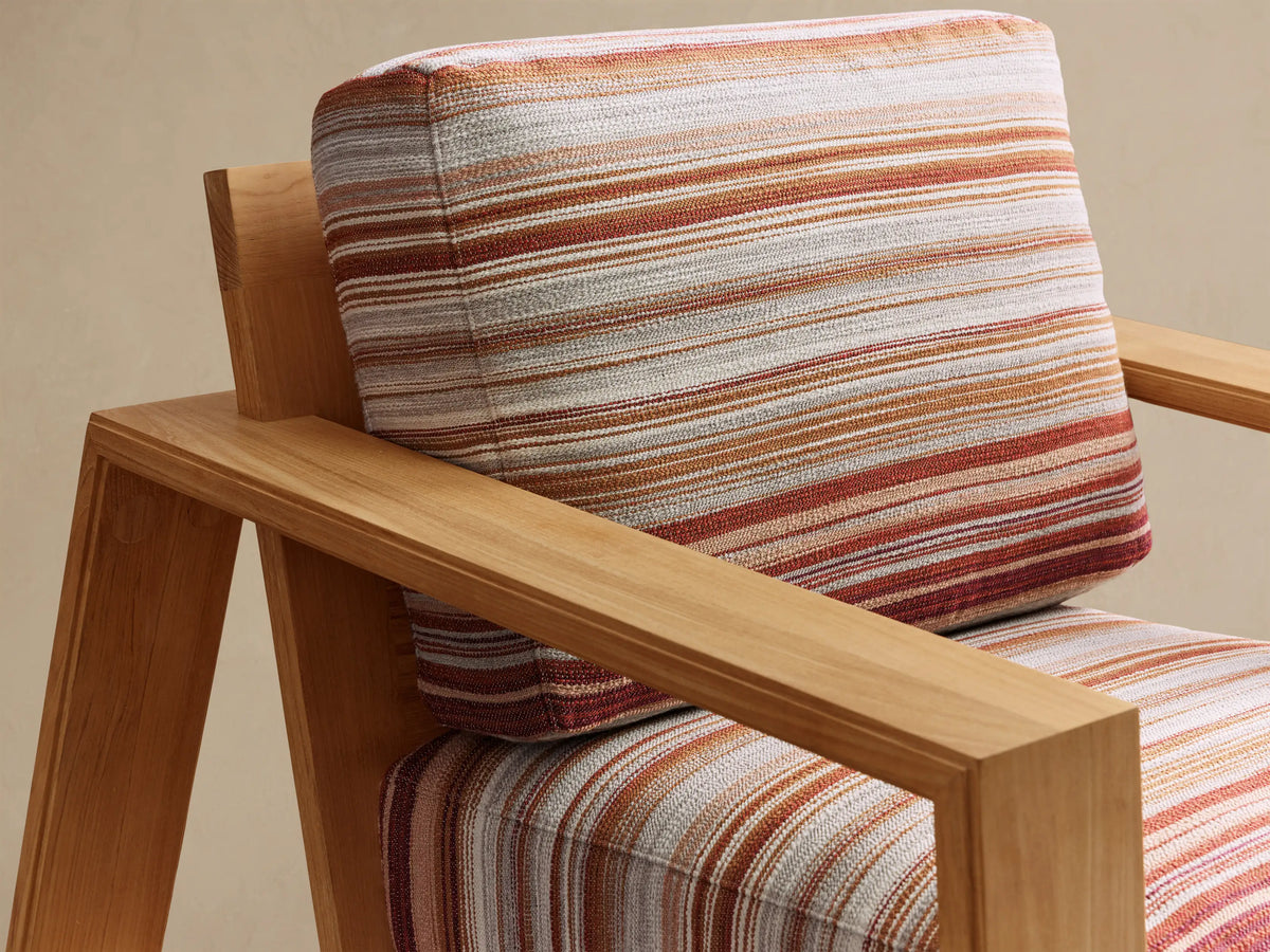 Close-up, angled view of the Canyon Outdoor Teak Lounge Chair, with natural teak frame and striped red, orange, grey cushions.