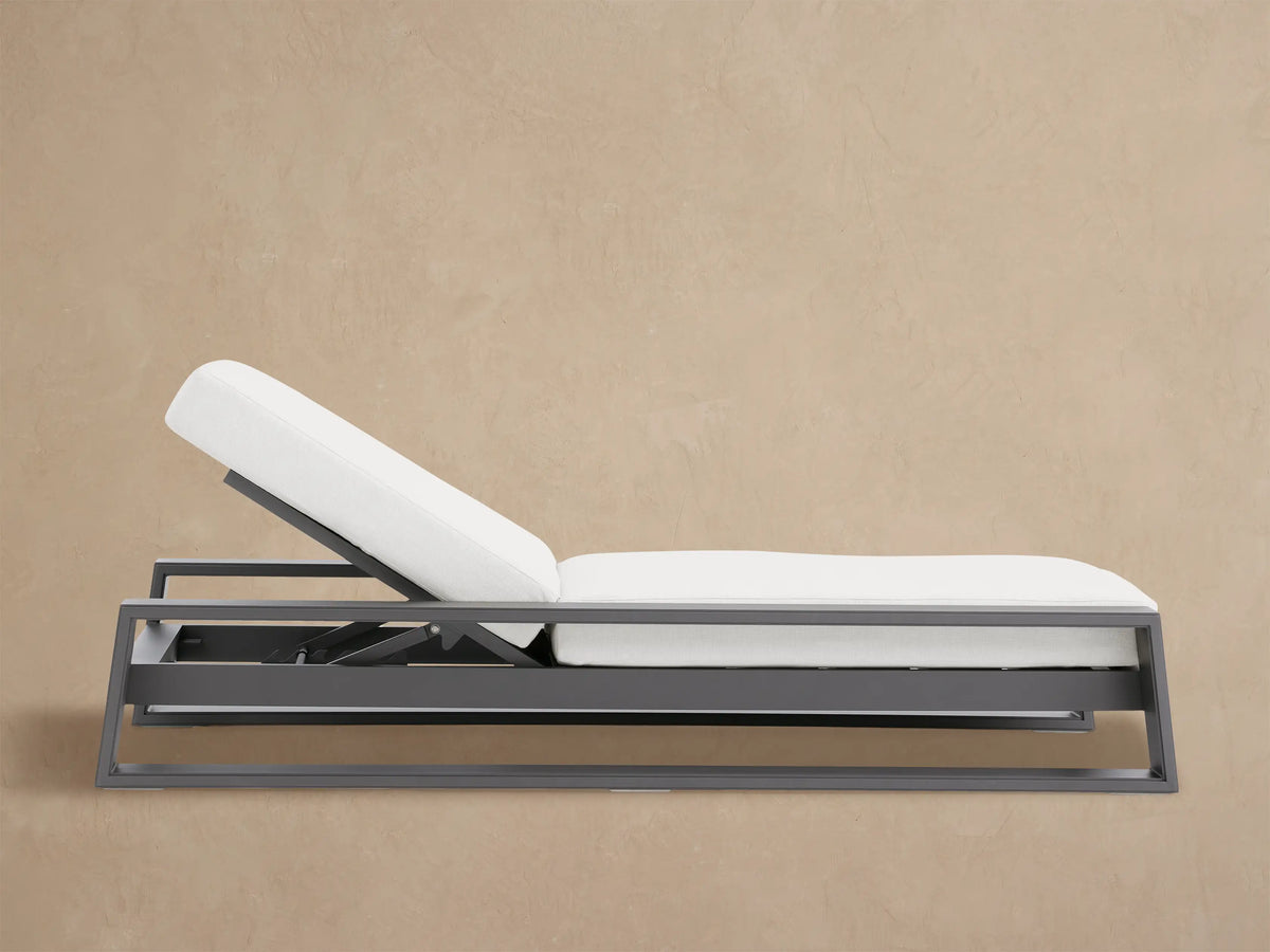 Canyon Outdoor Aluminum Chaise with gray frame and white cushions, headrest elevated, on a light-colored stone patio.