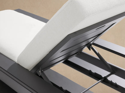 Side view of Canyon Outdoor Aluminum Chaise with dark gray frame and elevated backrest with white cushions against a tan wall.
