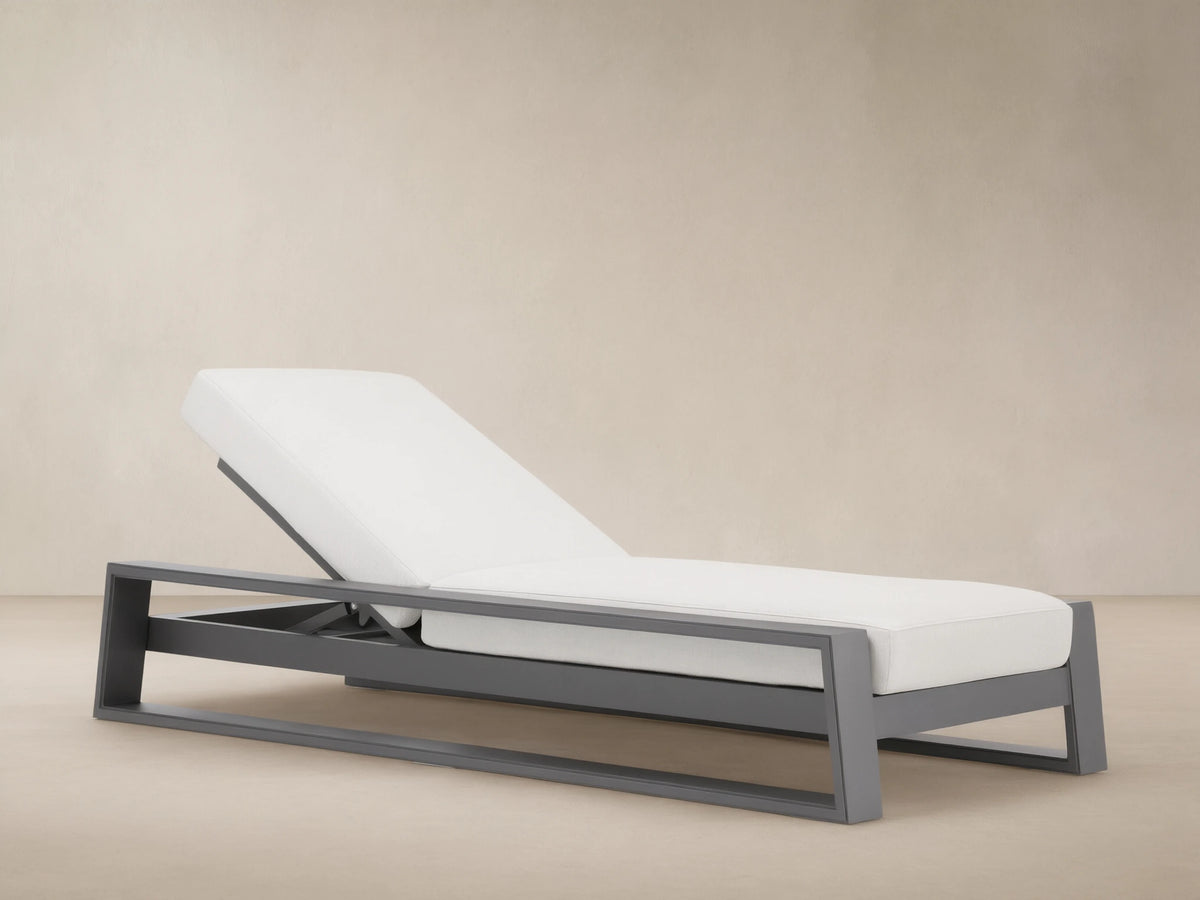 Canyon Outdoor Aluminum Chaise with gray frame and white cushions, headrest elevated, on a light-colored stone patio.