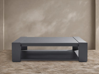 Canyon Outdoor Aluminum Coffee Table, rectangular, dark charcoal gray, slatted top and lower shelf, outdoors on a patio.