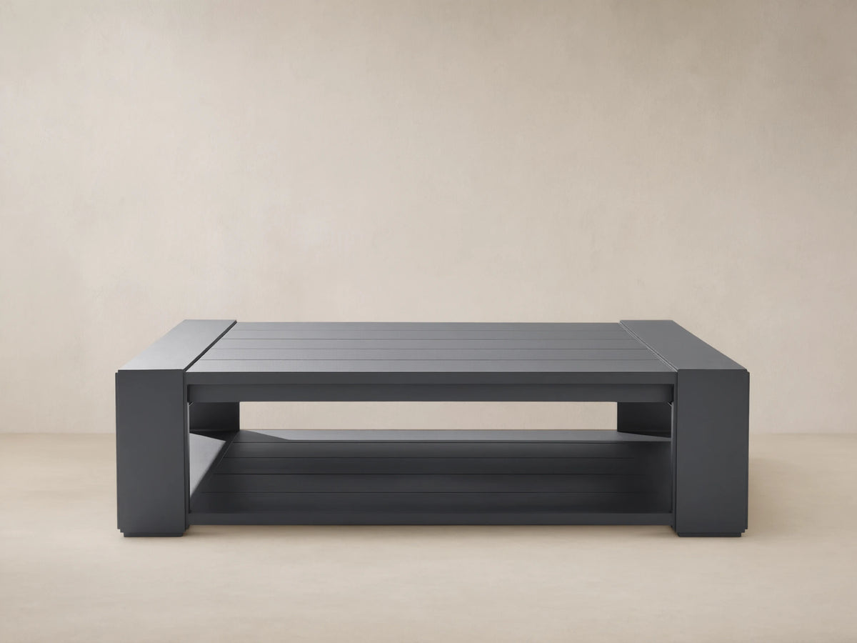 Canyon Outdoor Aluminum Coffee Table, rectangular, dark charcoal gray, slatted top and lower shelf, outdoors on a patio.