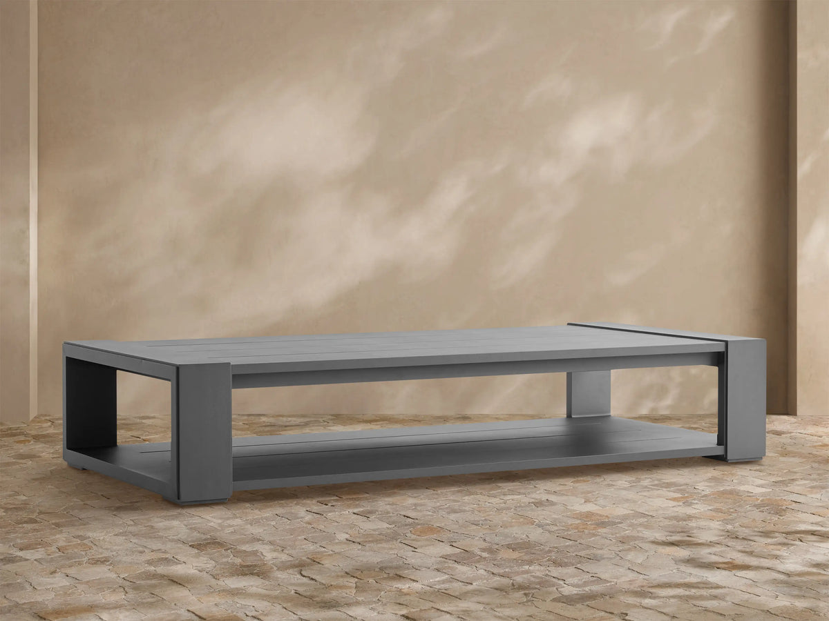 Charcoal Canyon Outdoor Aluminum Coffee Table, rectangular with slatted top and lower shelf, shown on stone patio.
