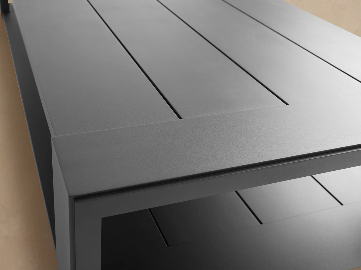 Canyon Outdoor Aluminum Coffee Table, dark gray rectangular with a slatted top and lower shelf, on a stone patio.