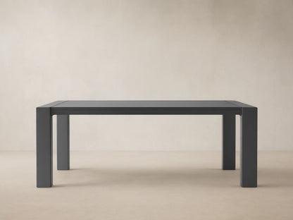 Dark gray rectangular Canyon Outdoor Aluminum Dining Table with slatted top and thick legs, on a light-colored paved patio.