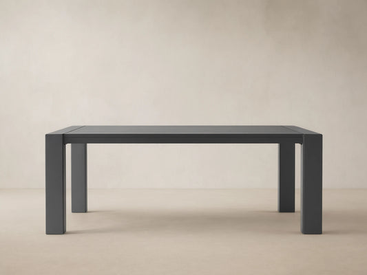 Dark gray rectangular Canyon Outdoor Aluminum Dining Table with slatted top and thick legs, on a light-colored paved patio.