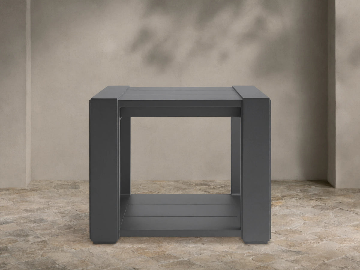 Dark grey square Canyon Outdoor End Table, aluminum with slat top & bottom shelf, on a stone patio.