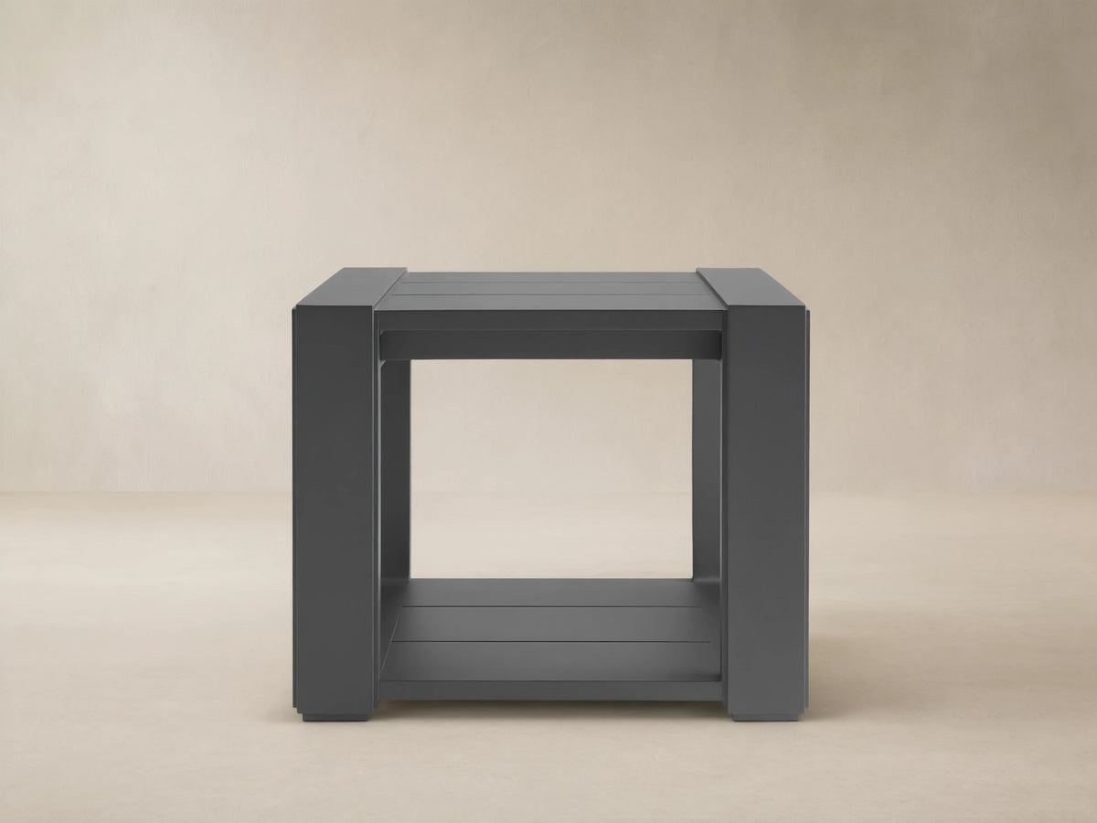 Dark grey square Canyon Outdoor End Table, aluminum with slat top & bottom shelf, on a stone patio.