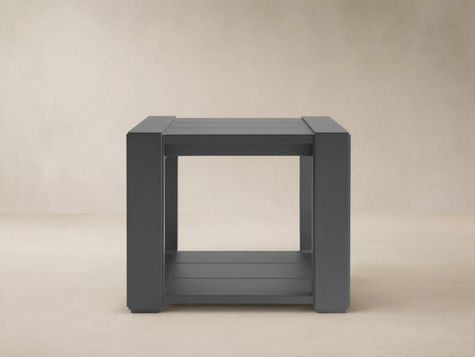 Dark grey square Canyon Outdoor End Table, aluminum with slat top & bottom shelf, on a stone patio.