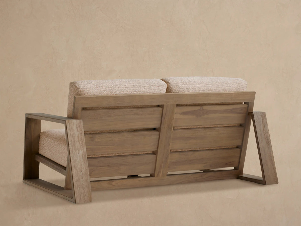 Close-up of Canyon Outdoor Teak Sofa from side angle, showing distressed silvery-grey teak frame and textured tan cushions.