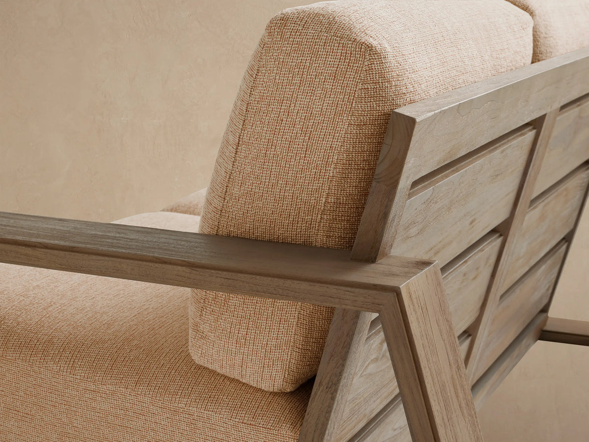 Canyon Outdoor Teak Sofa with weathered, angular teak frame and light beige cushions, set on a tiled patio against a light wall.