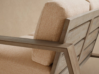 Canyon Outdoor Teak Sofa with weathered, angular teak frame and light beige cushions, set on a tiled patio against a light wall.