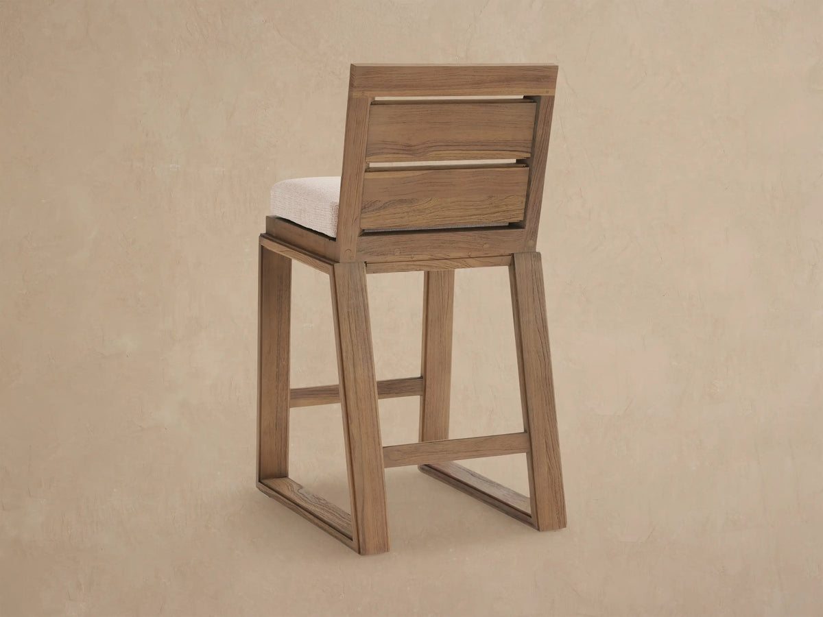 Close-up, angled view of a Canyon Outdoor Teak Barstool with distressed brownish-gray teak frame & light textured cushion.