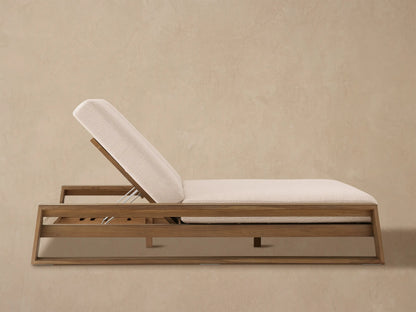 Canyon Outdoor Teak Double Chaise with light beige cushions on a stone patio against a tan wall, left backrest raised.
