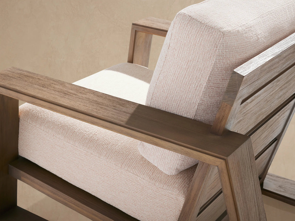 Canyon Outdoor Teak Lounge Chair, front view. Sturdy light brown teak frame with thick, light beige cushions on a stone patio.