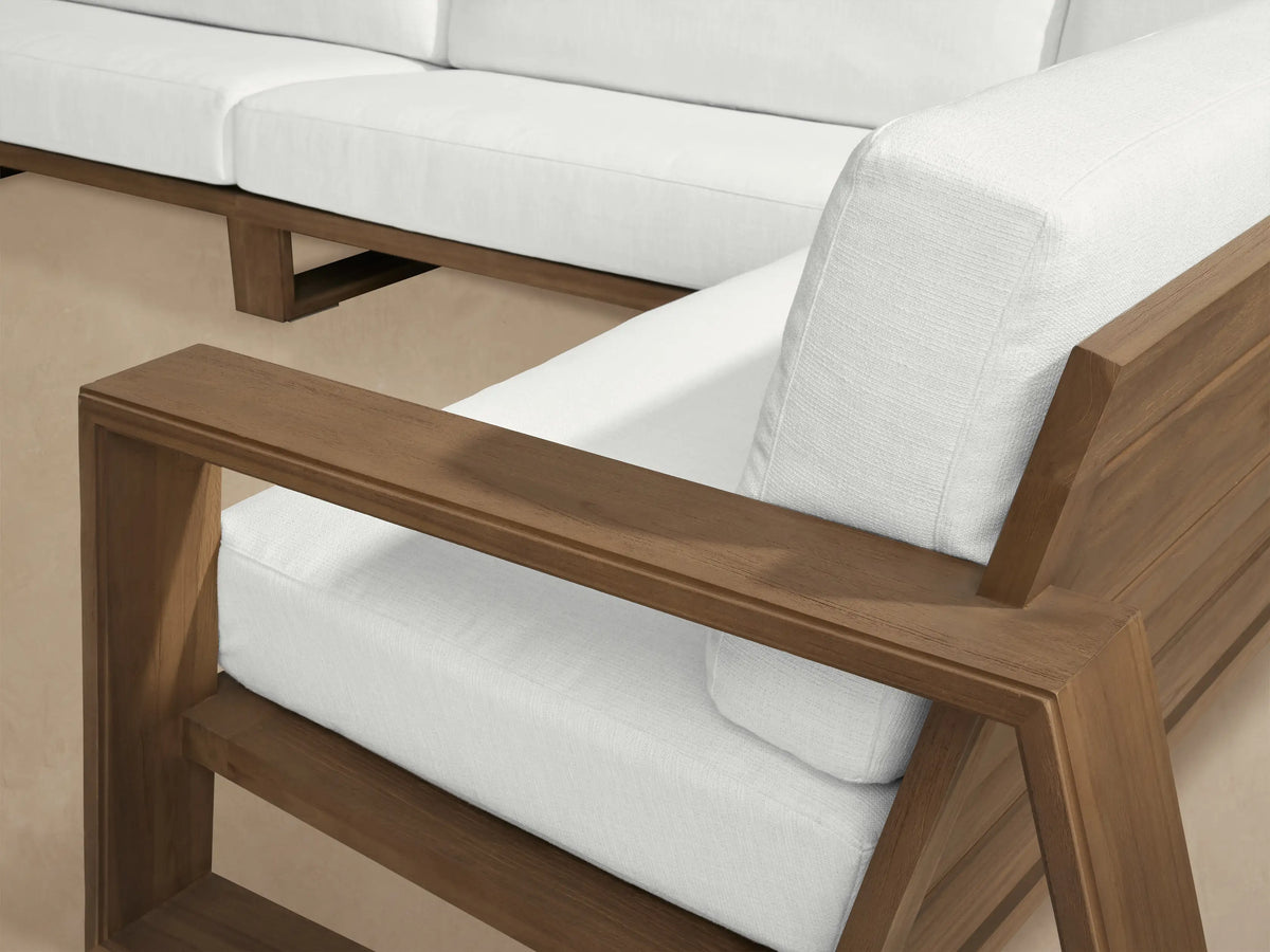 Canyon Outdoor Teak Four-Piece Sectional with dark teak wood frame & white cushions on a paved patio against a light wall.