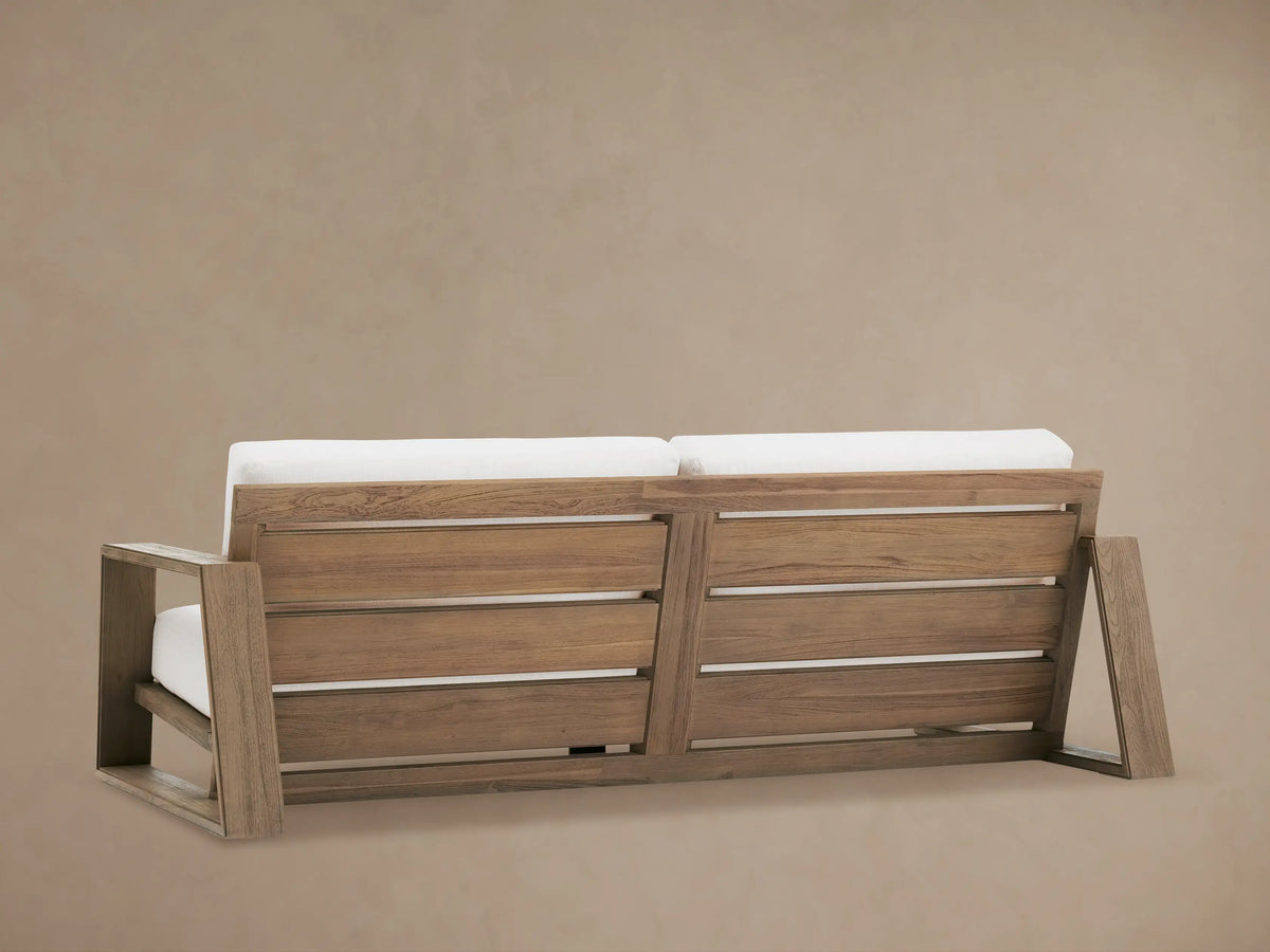 Close-up of Canyon Outdoor Teak Sofa: weathered teak armrest with visible grain and plush white outdoor cushions.