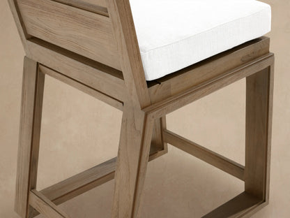 Canyon Outdoor Teak Barstool, light brown wood, white cushion, slatted backrest, front view, against a textured wall.