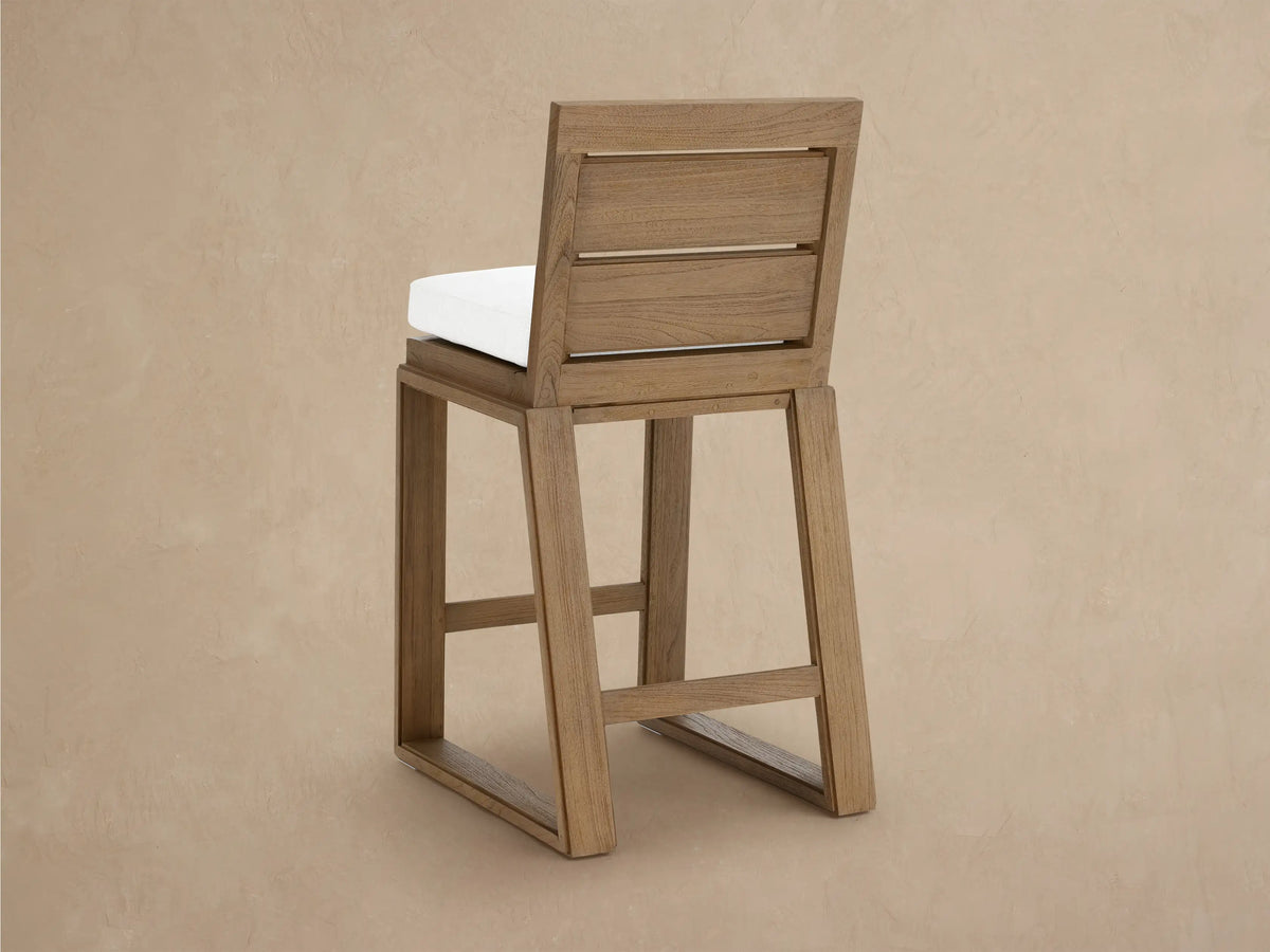 Angled close-up of a Canyon Outdoor Teak Barstool, featuring its distressed light brown teak wood frame and white seat cushion.