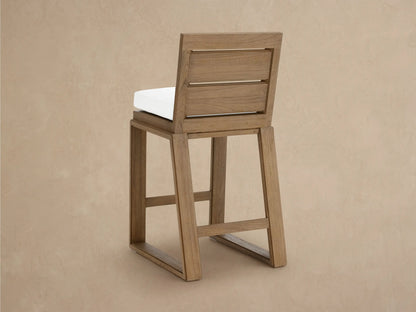 Angled close-up of a Canyon Outdoor Teak Barstool, featuring its distressed light brown teak wood frame and white seat cushion.