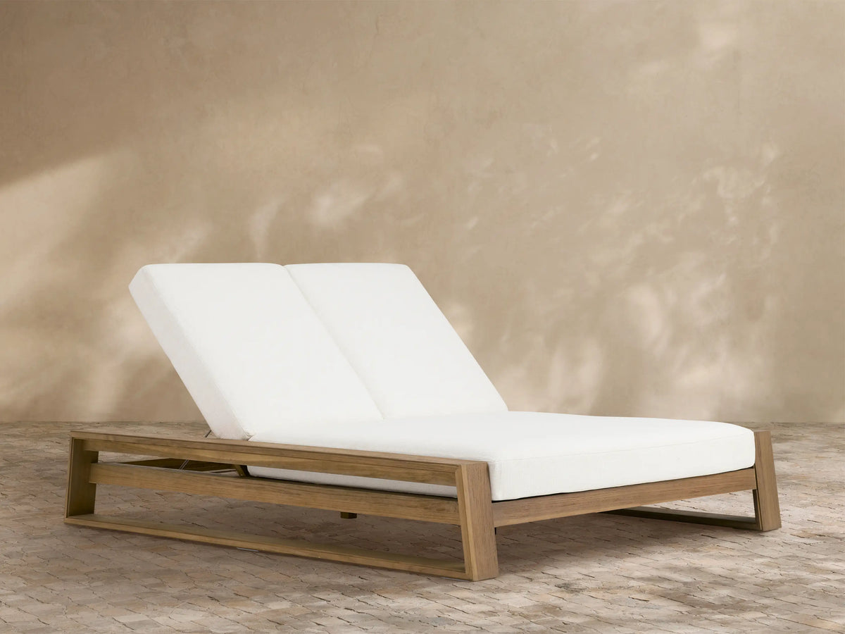 Canyon Outdoor Teak Double Chaise with light brown wood frame & white cushions. Backrests slightly raised, on a patio.