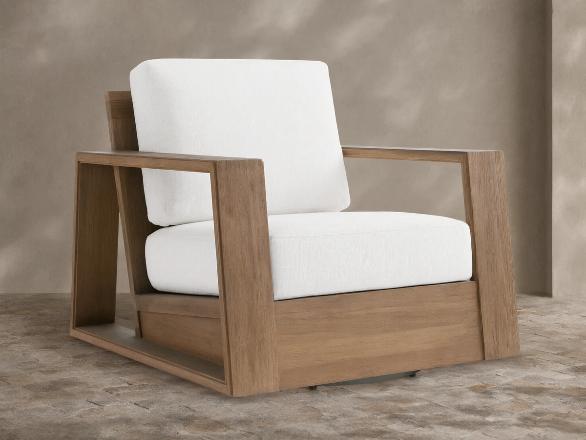 Canyon Outdoor Teak Swivel Chair with a modern, blocky natural teak frame & thick white cushions, angled on a tiled patio.