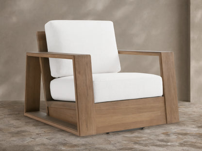 Canyon Outdoor Teak Swivel Chair with a modern, blocky natural teak frame & thick white cushions, angled on a tiled patio.