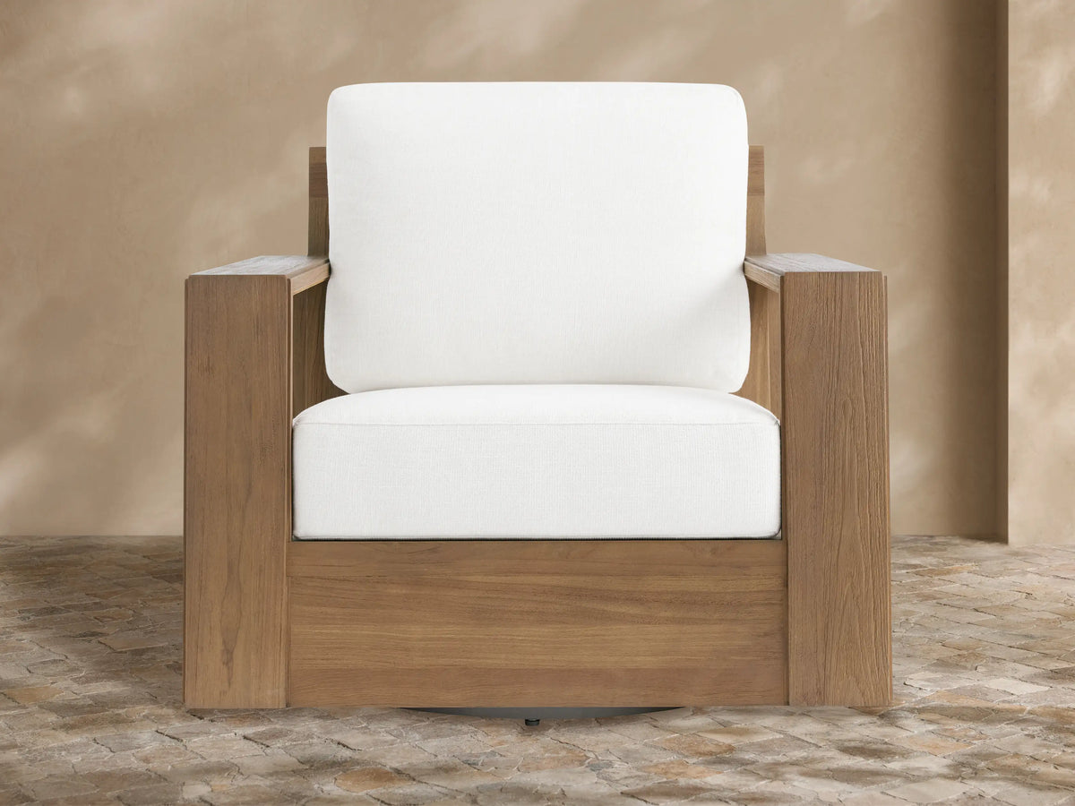 Canyon Outdoor Teak Swivel Chair with a modern, blocky natural teak frame & thick white cushions, angled on a tiled patio.