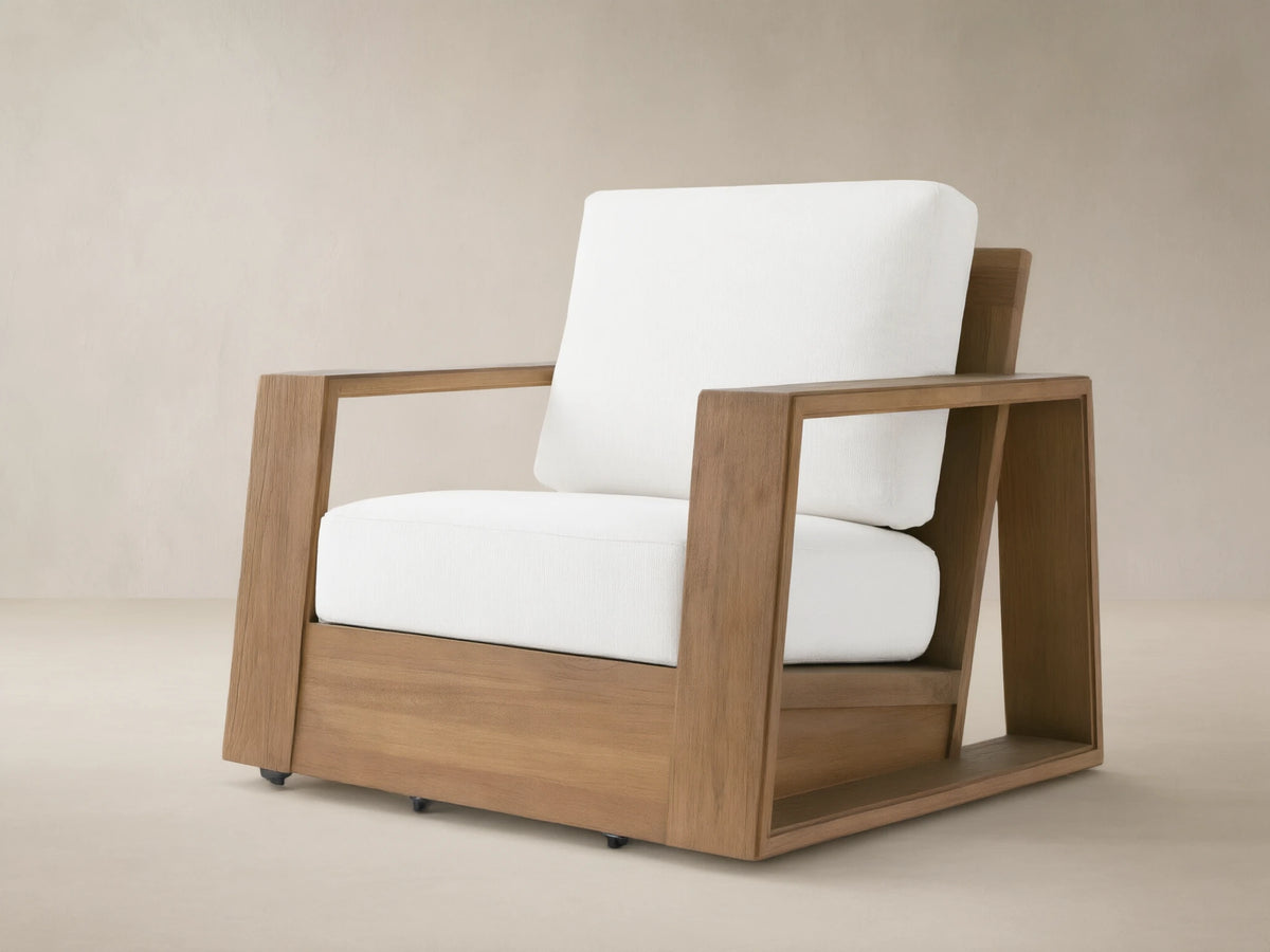 Canyon Outdoor Teak Swivel Chair with a modern, blocky natural teak frame & thick white cushions, angled on a tiled patio.