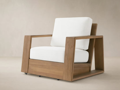 Canyon Outdoor Teak Swivel Chair with a modern, blocky natural teak frame & thick white cushions, angled on a tiled patio.