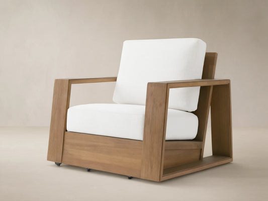 Canyon Outdoor Teak Swivel Chair with a modern, blocky natural teak frame & thick white cushions, angled on a tiled patio.
