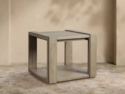 Weathered grey-brown square Canyon Outdoor Teak End Table, with slatted top and bottom shelf, on a stone patio.
