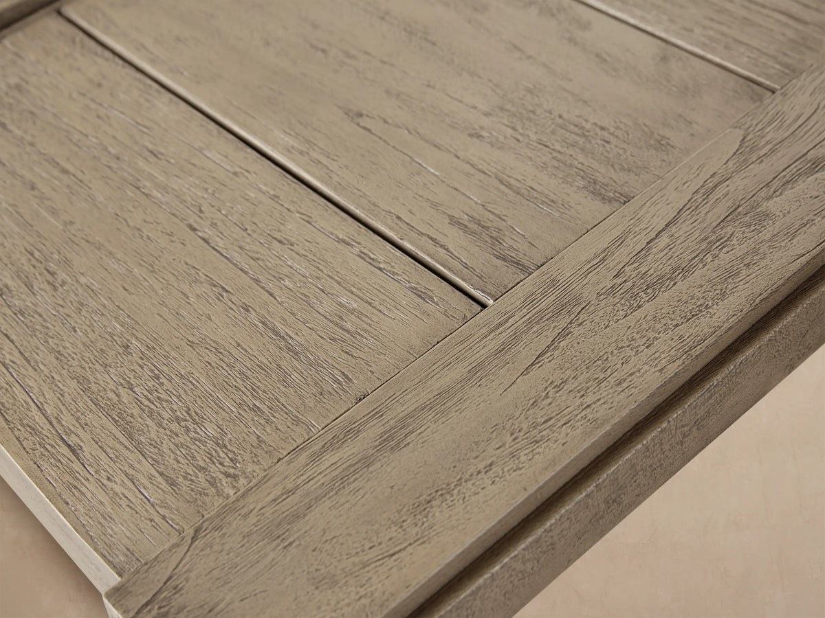Canyon Outdoor Teak End Table, square, two-tier, grey distressed teak, on a tiled patio against a beige wall.